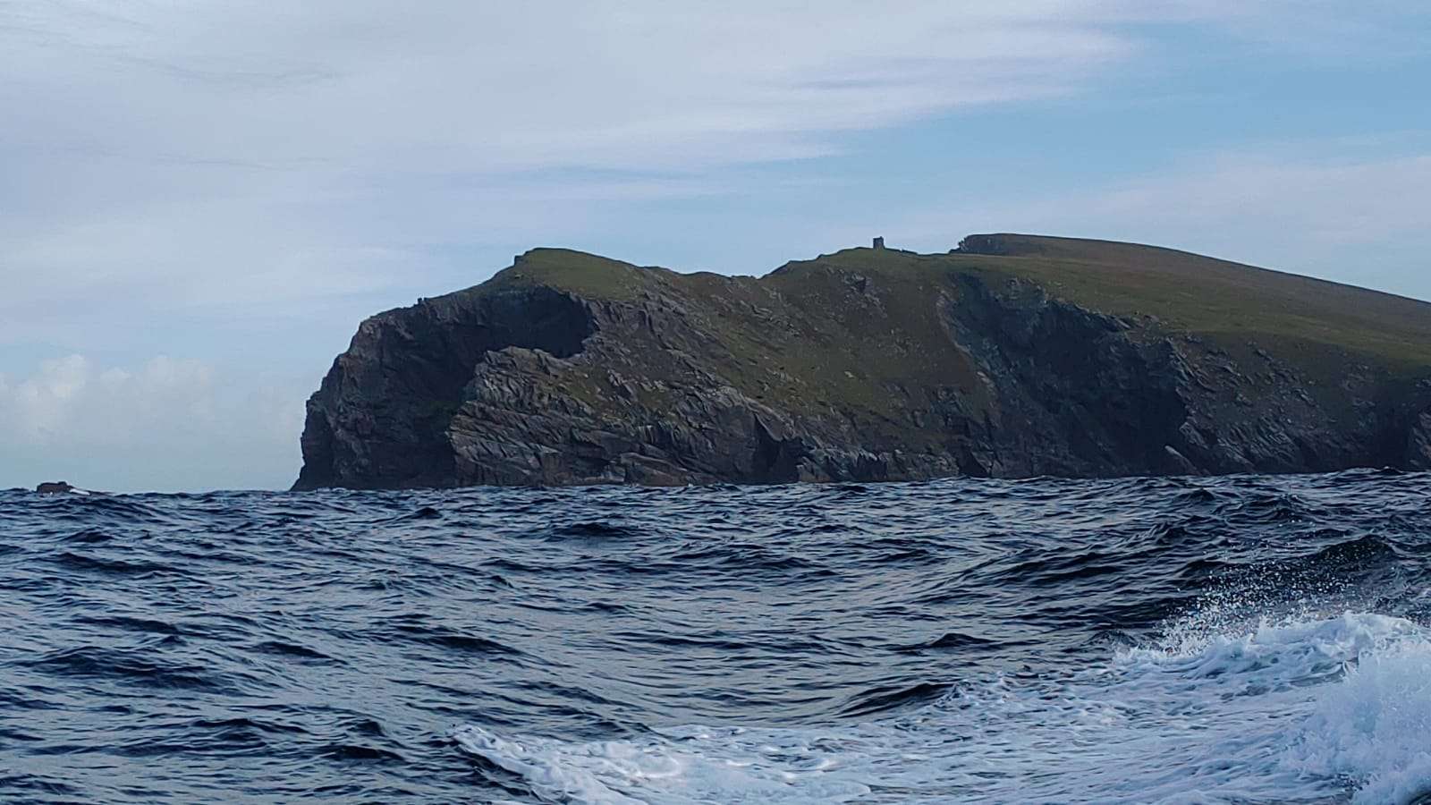 A green headland with a small tower on top, seen from the sea