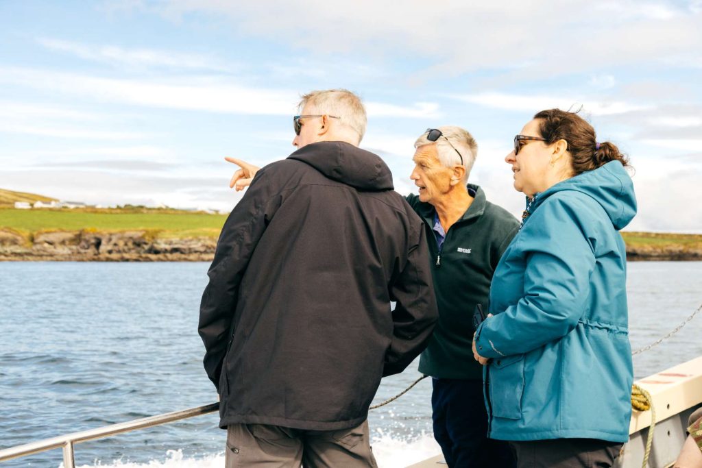 Three passengers on the boat, one pointing at the coast Three passengers on the boat, one pointing at the coast
